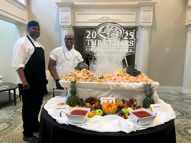 Cedars chefs standing beside a seafood and fruit display with an ice sculpture celebrating The Cedars of Chapel Hill.